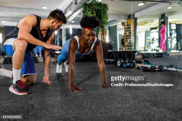 a young trainer is helping a female african athlete in a gym to work to do push-ups. - black female bodybuilder stock pictures, royalty-free photos & images