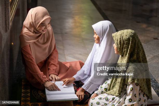 beautiful muslim girl in hijab teaching kids to read quran in mosque - koran stock pictures, royalty-free photos & images