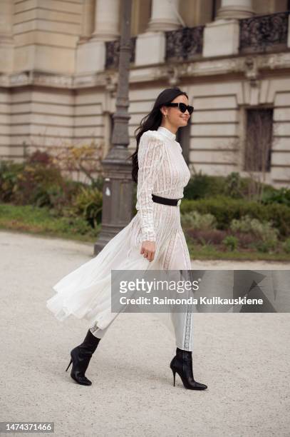 Kelsey Merrit is seen wearing a white semi sheer dress with a black belt, black sunglasses and black boots outside the Zimmermann show during Paris...