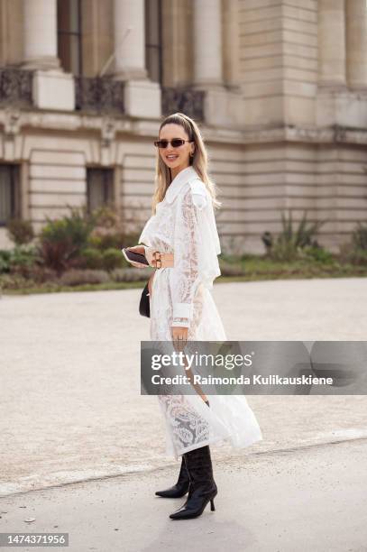 Guest seen wearing a white semi sheer dress, black long shoes, a black bag and sunglasses outside the Zimmermann show during Paris Fashion Week -...