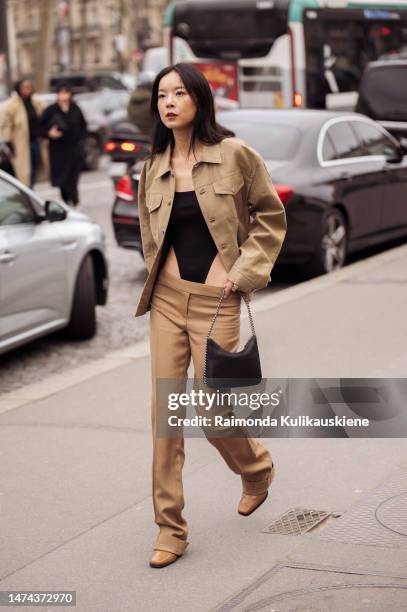 Guest wears gold earrings, a beige denim jacket, a black squared-neck / cut-out waist body top, brown flared suit pants, a black faux leather handbag...