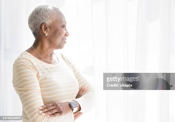 senior black woman thinking by the window - hearing aids stock pictures, royalty-free photos & images
