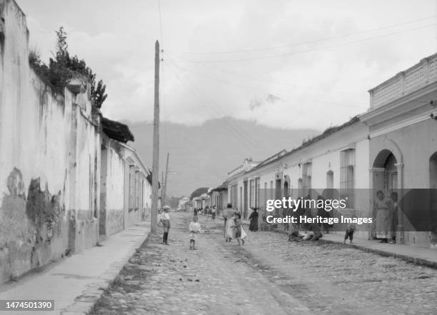 Travel views of Cuba and Guatemala, between 1899 and 1926. Street scene in Guatemala, volcano wreathed in clouds in the distance. Creator: Arnold...