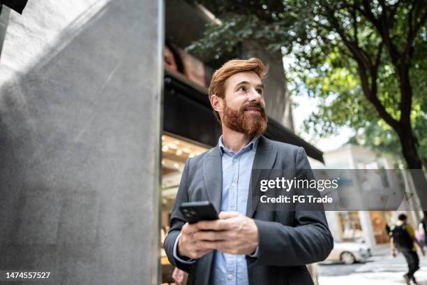 businessman using mobile phone and looking around outdoors - looking around stock pictures, royalty-free photos & images