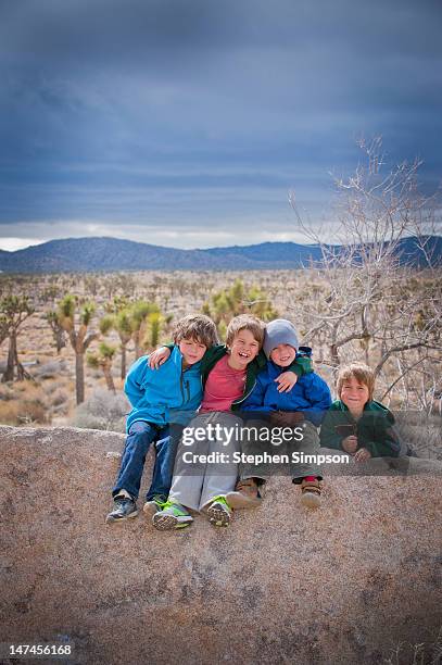 four boys on desert camping trip, winter - front view portrait of four children sitting on rock stock pictures, royalty-free photos & images