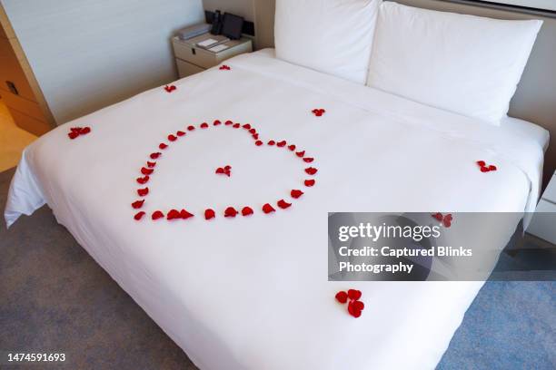 hotel bed with rose petals in heart shape for romantic holiday or honeymoon - secluded couple stockfoto's en -beelden