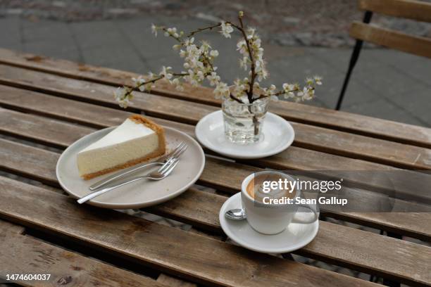 Slice of cheesecake and a cup of espresso macchiato coffee stand on an outdoor table at a cafe on March 19, 2023 in Berlin, Germany. The German...