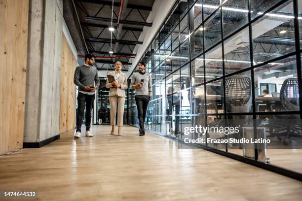 coworkers talking while walking through corridor at office - corridor bildbanksfoton och bilder