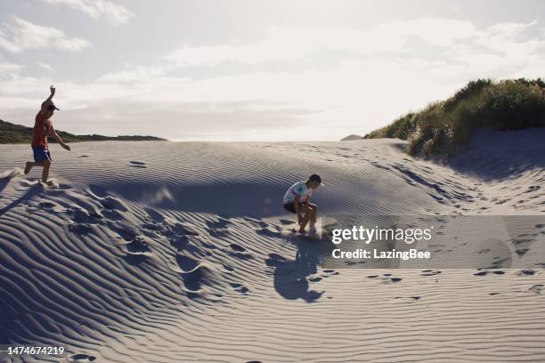 boys jumping in sand dunes in evening beach scene - new zealand beach stock pictures, royalty-free photos & images