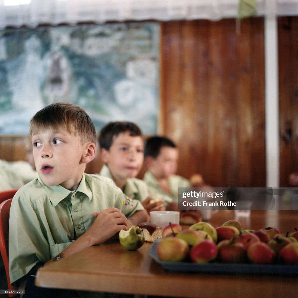 A young boy eats an apple on a big table