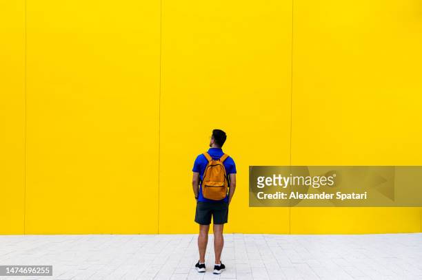 rear view of a man with backpack against yellow wall - calções azuis - fotografias e filmes do acervo