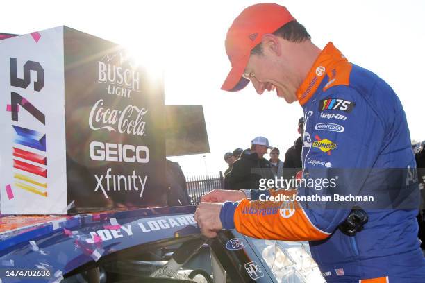 Joey Logano, driver of the Autotrader Ford, places the winner sticker on his car in victory lane after winning the NASCAR Cup Series Ambetter Health...