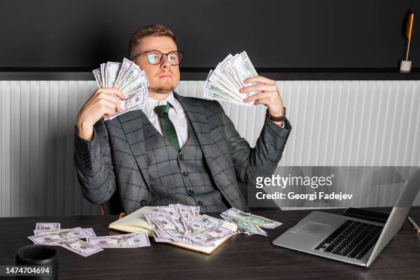 a young serious man in a gray formal suit and glasses sits at his desk and counts cash. a businessman holds money. - asset photos et images de collection