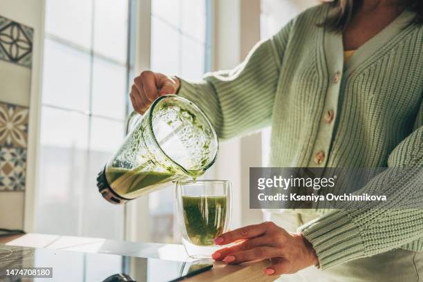 young woman making detox smoothie at home. woman pouring smoothie to glass. healthy food concept - smoothies stockfoto's en -beelden