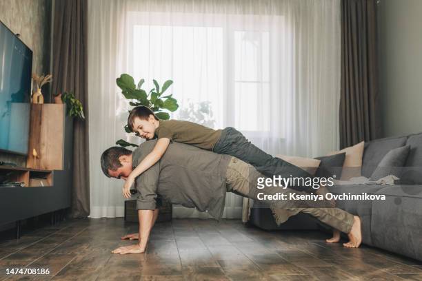 happy father doing push up exercise with son on back at gym. little boy hugs dad from behind - dad press ups kids stock pictures, royalty-free photos & images