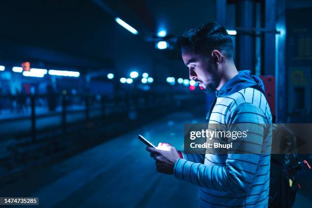 young man using a smartphone while waiting for the train. - plataforma de estação de metro imagens e fotografias de stock