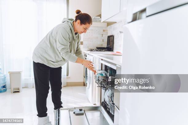 daily routine, chores. female cleaning, washing the dishes with dish washing machine at home - vaatwastablet stockfoto's en -beelden