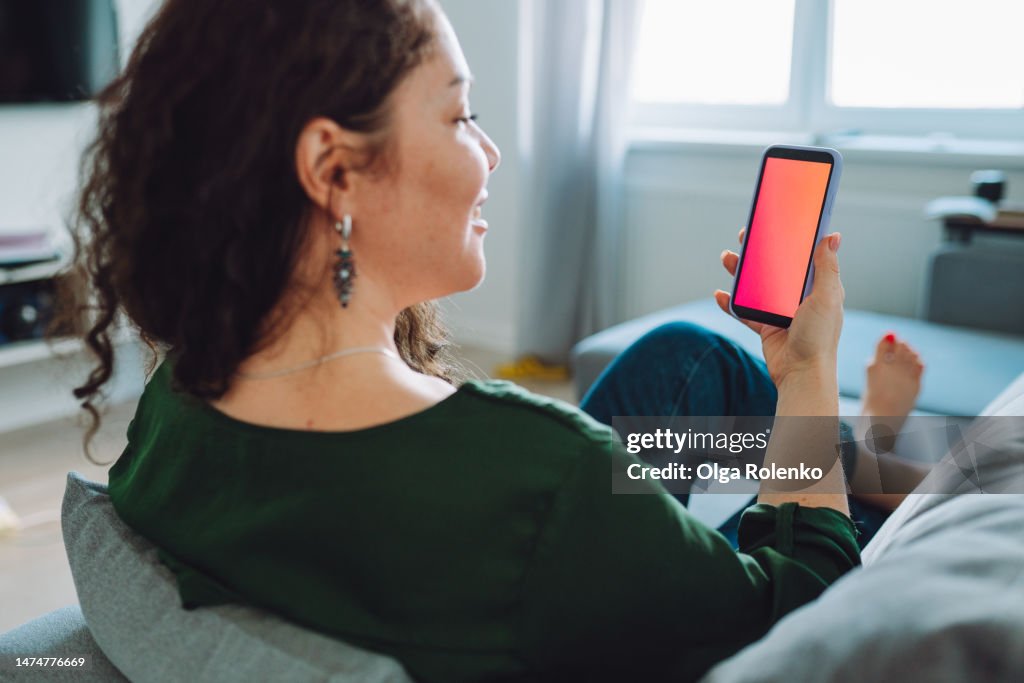 Rearview of brunette woman using mobile application on a smartphone with red blank display
