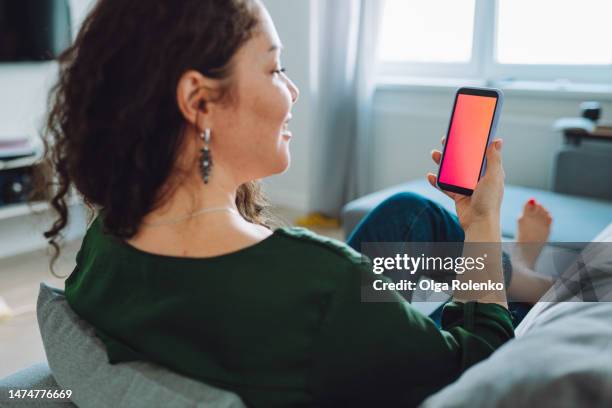 rearview of brunette woman using mobile application on a smartphone with red blank display - looking over shoulder stock pictures, royalty-free photos & images