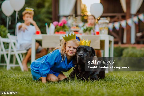 cute birthday girl holds labrador retriever against party friends background. - picknick kid stock pictures, royalty-free photos & images