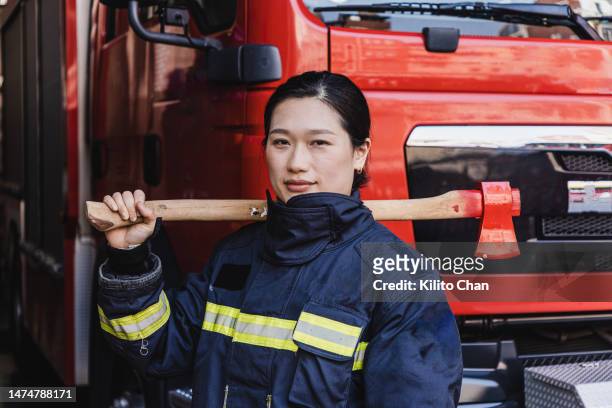 asian female fire fighter holding an axe standing in front of a fire truck - fireman axe stock pictures, royalty-free photos & images