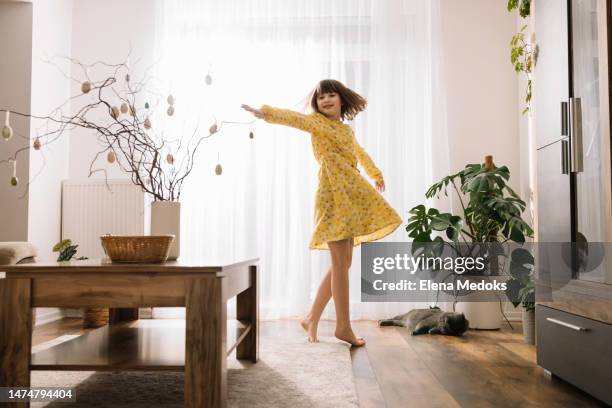 a happy teenage girl dances in a sunny room next to sprigs decorated with easter eggs in a vase. happy childhood and carelessness - easter decoration home stock pictures, royalty-free photos & images