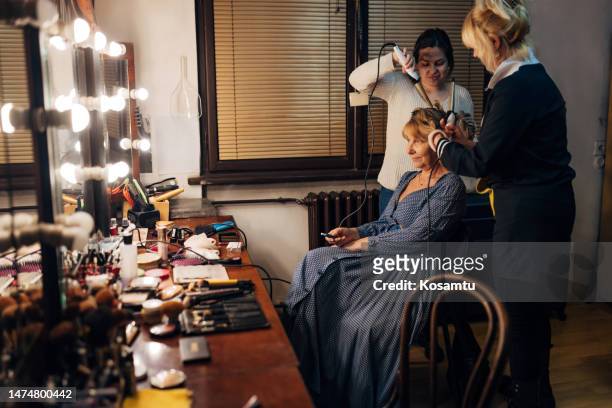 side view of senior actress preparing for theater performance, hairdresser and make-up artist doing her hair and make-up - celebrity event stock pictures, royalty-free photos & images