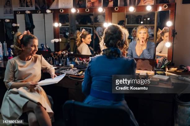 a senior actress applies lipstick, while her colleague sits next to her and reads the text of the play - creative makeup stockfoto's en -beelden