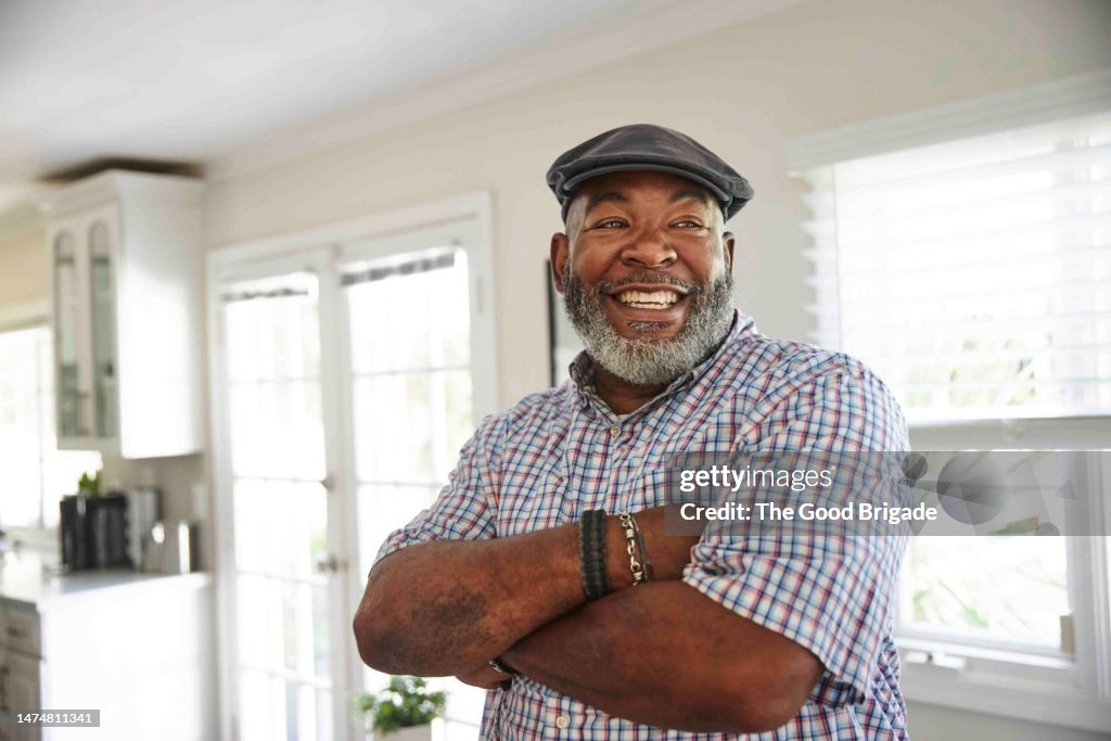 Portrait of mature man with beard standing with arms crossed at home