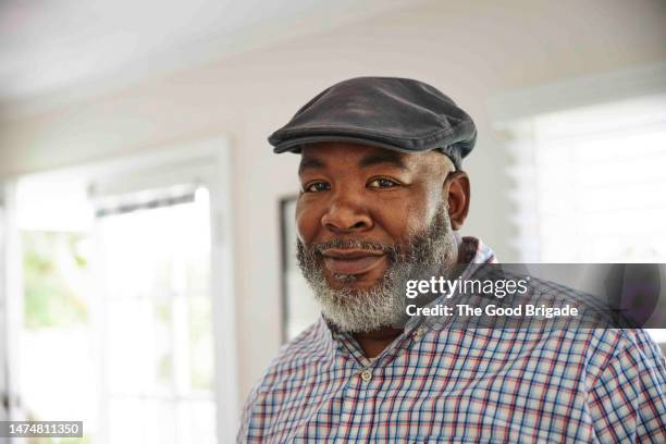 portrait of smiling mature man wearing flat cap at home - baker boy cap stock-fotos und bilder