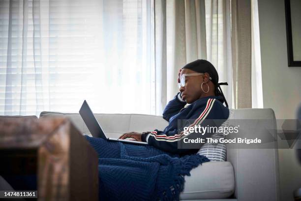 woman battling cancer using laptop while reclining on sofa at home - survival blanket stock pictures, royalty-free photos & images