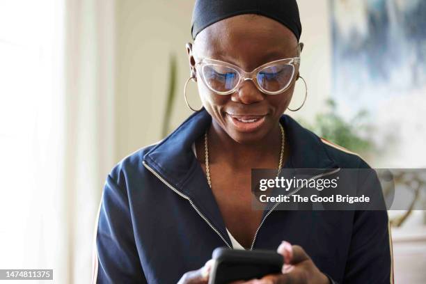 woman with cancer wearing eyeglasses using mobile phone at home - cellphone cancer illness stock-fotos und bilder