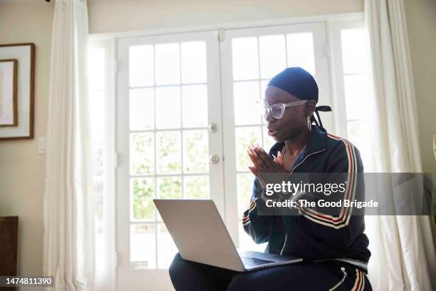 female cancer patient with hands clasped doing video call on laptop at home - business enterprise survival endurance stock pictures, royalty-free photos & images