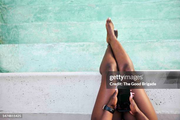 directly above shot of woman holding smart phone while sitting by swimming pool - 足首を重ねる ストックフォトと画像