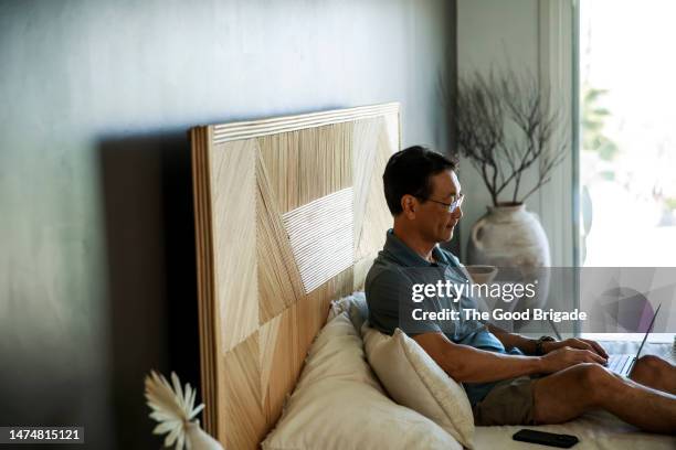 mature man using laptop while sitting on bed during vacation - headboard ストックフォトと画像