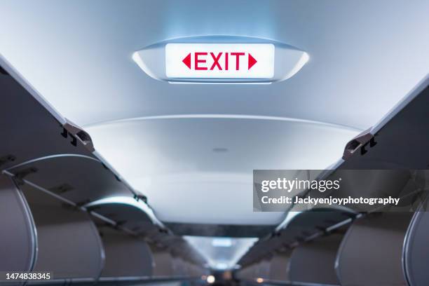 emergency exit sign on ceiling inside passenger aircraft cabin - sortir du rang photos et images de collection