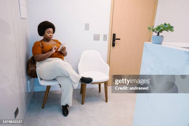 paciente en sala de espera usando teléfono inteligente - waiting room fotografías e imágenes de stock