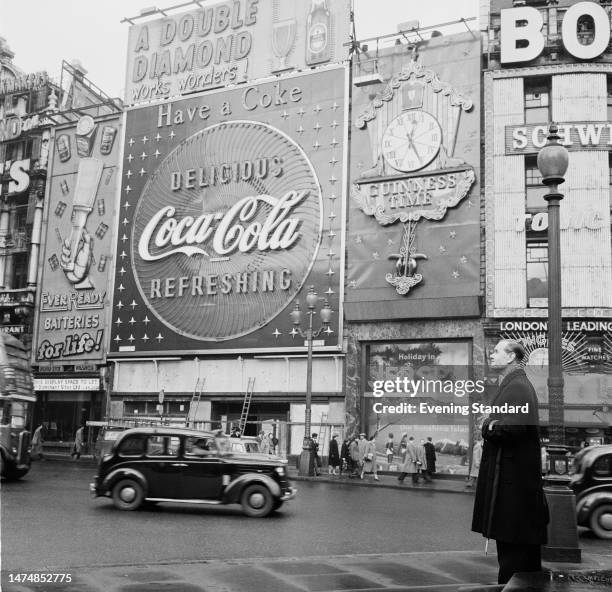 Man stands opposite the Coca-Cola and Guinness clock advertising hoardings at Piccadilly Circus, London, January 20th, 1960.