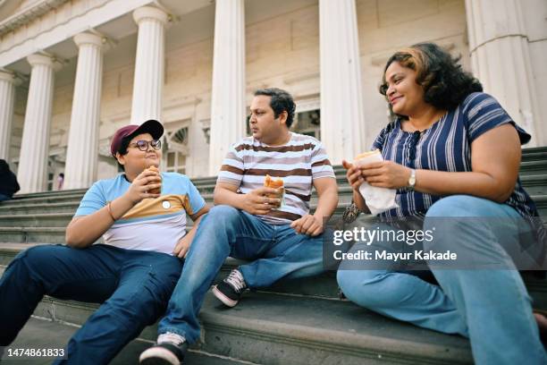 family with a teenage son enjoying street food sitting on the steps - indian family in their 40's with kids imagens e fotografias de stock