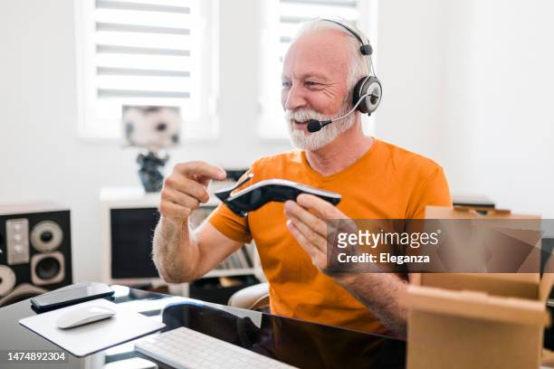 smiling senior male social media technology influencer with headset recording unboxing video at home - toiletries stock pictures, royalty-free photos & images