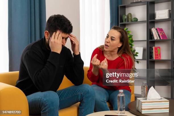 young heterosexual couple arguing while sitting on sofa at home. - complaining stock pictures, royalty-free photos & images