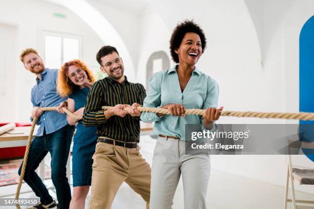 playful entrepreneurs playing tug-of-war in the office - adult sports team stock pictures, royalty-free photos & images