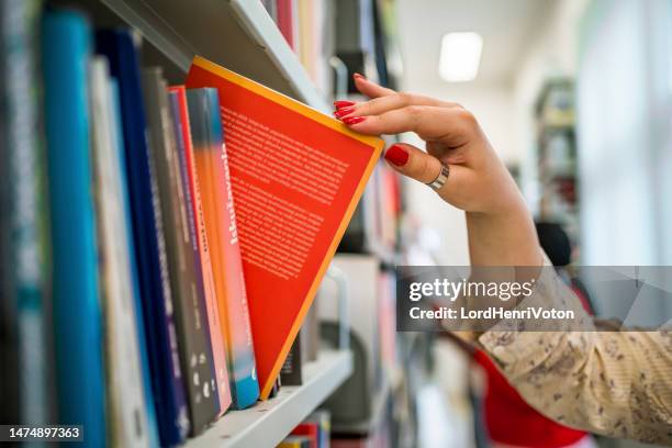 mano della donna che raccoglie un libro da una libreria della biblioteca - bibliotecario foto e immagini stock