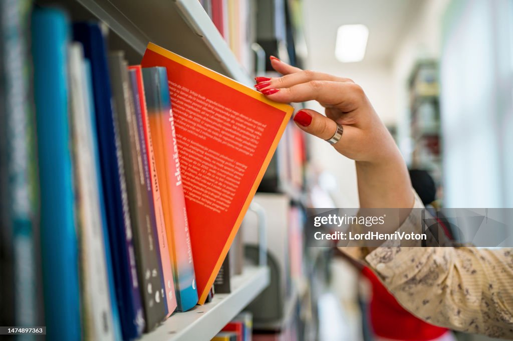 Woman's hand picking a book from a library bookshelf