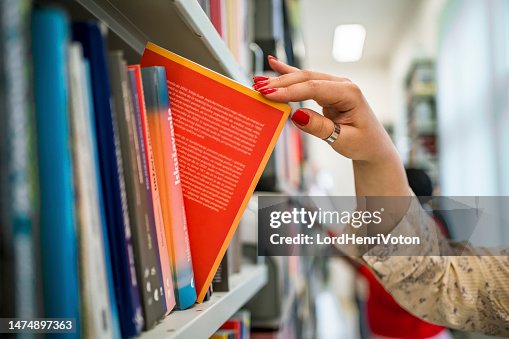 Woman's hand picking a book from a library bookshelf Woman's hand picking a book from a library bookshelf