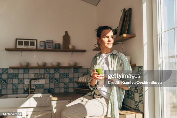 young woman drinking healthy green smoothie in kitchen - drinking juice stock-fotos und bilder