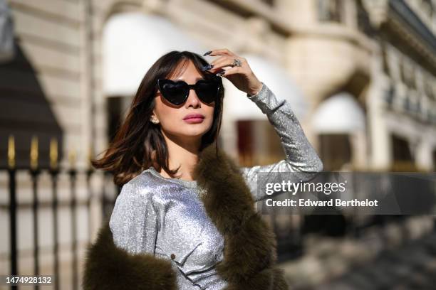 Heart Evangelista wears heart-shaped sunglasses, a green khaki faux fur long winter coat, a silver shiny glitter dress / gown from Paco Rabanne,...