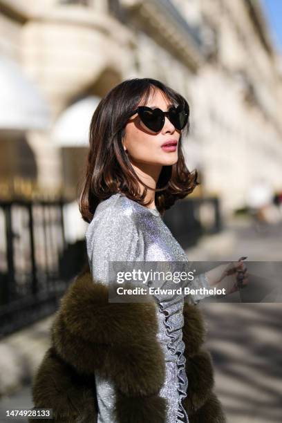 Heart Evangelista wears heart-shaped sunglasses, a green khaki faux fur long winter coat, a silver shiny glitter dress / gown from Paco Rabanne,...