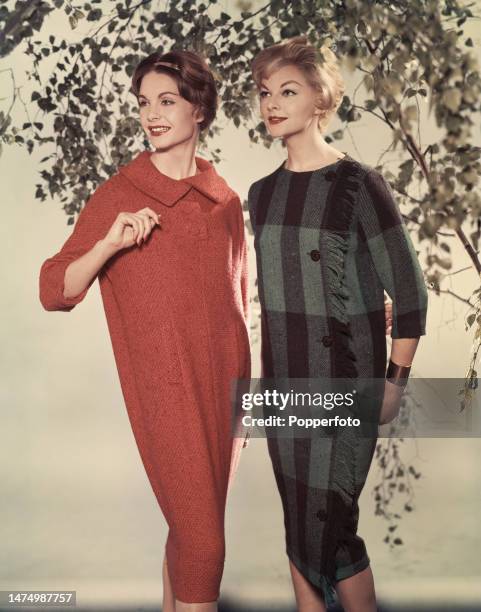 Posed studio portrait of two female fashion models wearing knee length straight dresses with tapered hems, one in red tweed and one in black and grey...