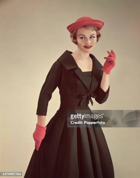 Posed studio portrait of a female fashion model wearing a black New Look style dress with sailor style collar, cinched waist and full skirt, red...